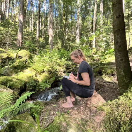 Frau sitzt auf einem Stein im Wald und macht sich Notizen